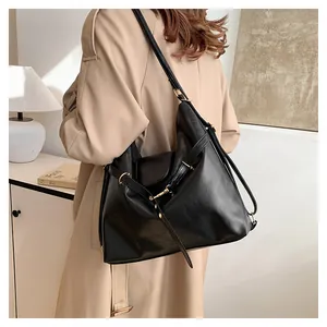 Detail of black faux leather tote bag with fine texture and gold buckle on beige coat