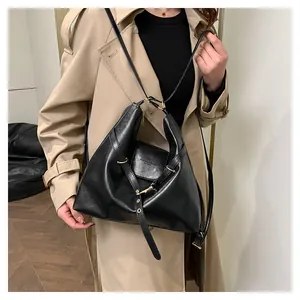 Detail of minimalist black PU leather tote with gold buckle and embossed text on beige coat