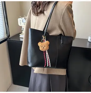 Side view of a large black leather tote bag with a plush bear charm on a female model