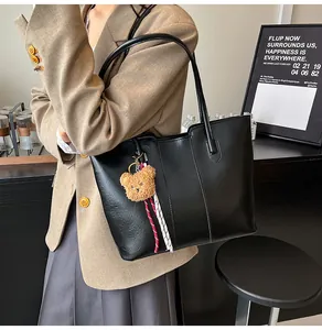 Detail of black faux leather tote bag featuring a cute brown bear plush charm and dual straps