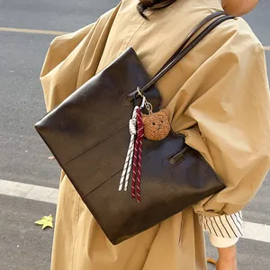 Brown leather tote bag with braided tassels and plush bear pendant in a street style view