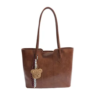 Brown leather tote bag with vertical stitching and cute bear charm ornament