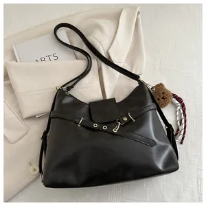 Close-up of black leather handbag with gold buckle, cross straps and cute bear charm