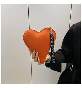 Gros plan sur un mini sac à main cœur orange avec bandoulière large imprimée LOVE