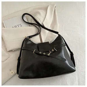 Detail of black PU leather tote bag with gold hardware on beige blazer background