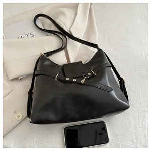 Detail view of the black leather crossbody bag with metal eyelet strap and smartphone for scale