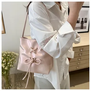 Détail d'un sac seau rose clair avec nœud ruban et œillets métalliques sur chemise
