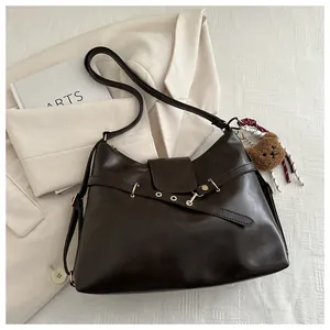 Detail view of deep brown leather tote bag with gold buckle and plush bear charm