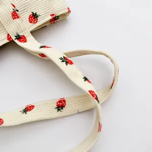 Detailed close-up of corduroy shoulder strap featuring sweet red strawberry print patterns