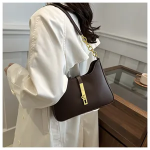 Détail du sac sous le bras en cuir marron foncé avec boucle dorée sur un manteau blanc