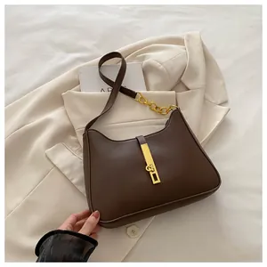Gros plan d'un sac porté épaule en cuir marron avec chaîne dorée sur un blazer beige