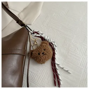 Detailed close-up of a brown fluffy bear charm with a woven strap on a leather handbag