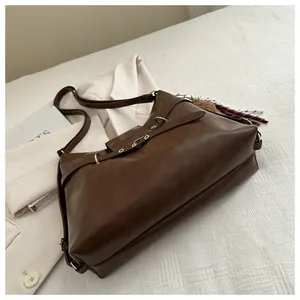 Detail of dark brown leather tote bag featuring a striped rope charm and adjustable strap