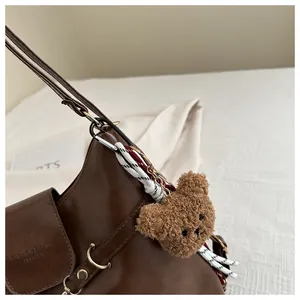 Detail view of brown leather bag with golden ring hardware and cute plush bear charm