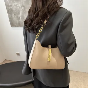 Sac à bandoulière beige chic avec chaîne dorée et boucle métallique porté par un modèle