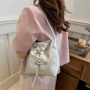 Sac seau métallisé argenté avec nœud décoratif porté à l'épaule par un mannequin