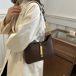 Sac sous le bras en cuir marron minimaliste avec fermoir doré sur un trench-coat chic