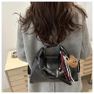Detail of black leather tote bag with plush bear charm and striped scarf on model back