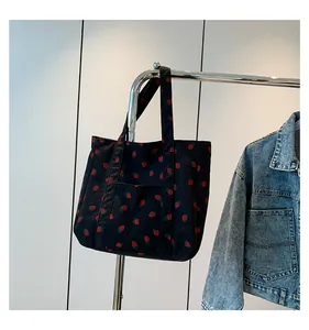 Detail of black corduroy tote bag with strawberry print hanging on a metal rack