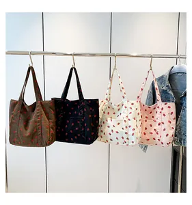 Multiple colors of large strawberry print corduroy tote bags hanging on display