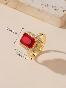 Détail macro d'une bague dorée réglable avec une grande pierre rouge et des oxydes de zirconium