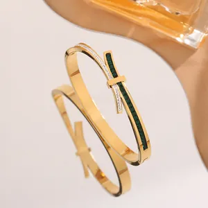 Gold bow-style titanium steel bangle with white diamonds and emerald green crystals