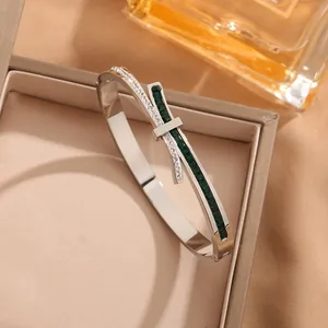 Silver titanium steel bow bangle with emerald square stones and pave diamonds in a box