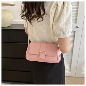 Détail du sac à bandoulière rose avec boucle dorée porté par un mannequin en intérieur