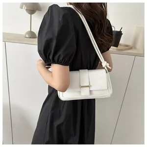 Détail d'un sac à bandoulière minimaliste en cuir blanc porté avec une robe noire chic
