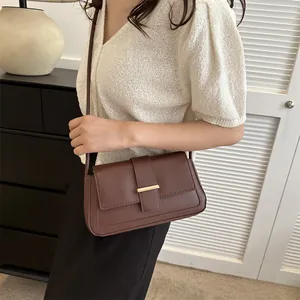 Petit sac bandoulière marron café avec fermoir doré présenté dans un décor intérieur
