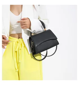 Détail d'un sac noir en similicuir avec poignée tressée et boucles dorées sur modèle