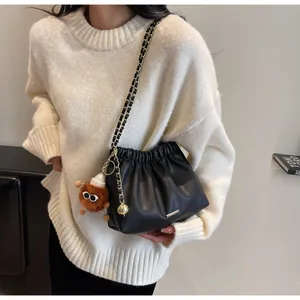 Close-up of black pleated bucket bag with gold chain strap and brown plush charm