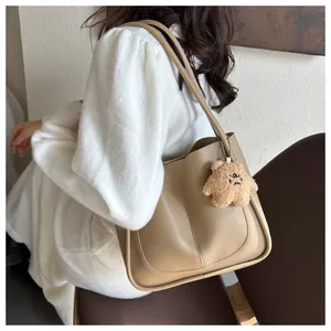 Beige tote bag with plush bear charm and vertical stitching detail on model