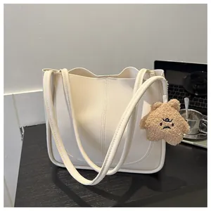 Detail of cream white faux leather tote bag with plush charm on a wooden desk