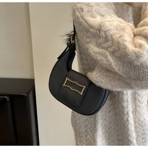 Détail d'un sac demi-lune noir avec boucle dorée sur un pull en maille blanc
