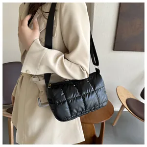 Détail d'un sac bandoulière matelassé noir brillant assorti à un trench-coat beige