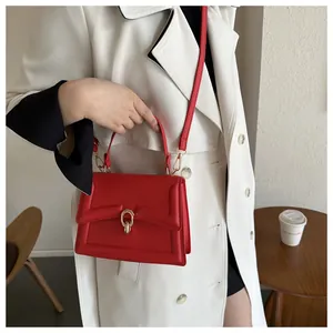 Close-up of bright red leather handbag with elegant gold oval buckle and thin shoulder strap