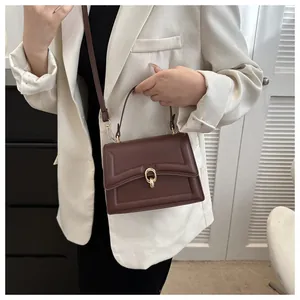 Detail of a dark brown leather handbag with a gold double ring buckle and slim strap