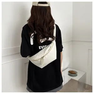 Detail view of a white crescent crossbody bag worn by a model in a minimalist setting