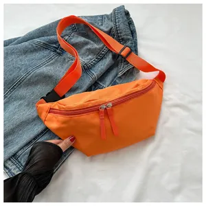 Detail view of vibrant orange nylon crossbody bag with dual zippers on denim background