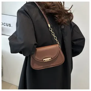Detail view of a brown leather shoulder bag with a gold cylindrical buckle and chain strap