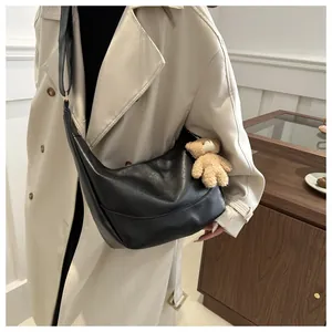 Model wearing a black soft leather crescent shoulder bag with a cute bear charm accessory
