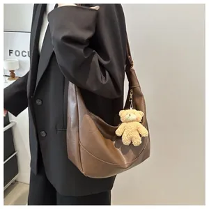 Detail of deep brown large hobo bag with a cute plush bear charm on a model's shoulder