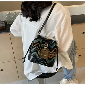 Detail view of woven bucket bag with colorful wavy pattern and black leather strap