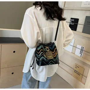 Detail view of woven bucket bag featuring multicolor wave pattern and black leather trim