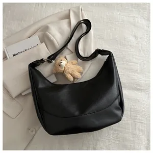 Detail of black pebbled leather half-moon bag featuring a cute brown plush bear charm
