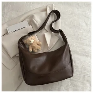 Detail view of dark brown crescent bag on white fabric with a plush bear charm