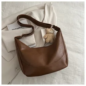 Detail of a brown PU leather crescent shoulder bag with a cute plush bear charm decoration