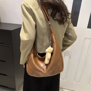 Brown leather half-moon shoulder bag with plush bear charm worn on a model