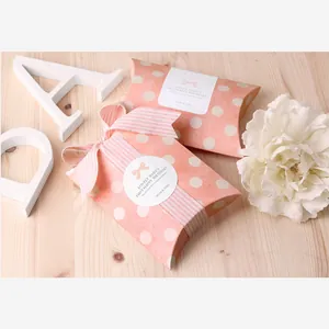 Gros plan sur la boîte cadeau polochon rose à pois avec ruban rayé et étiquette bébé